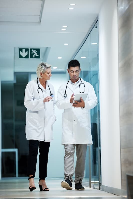 Two doctors reviewing data on a tablet as they walk through a hospital's corridor