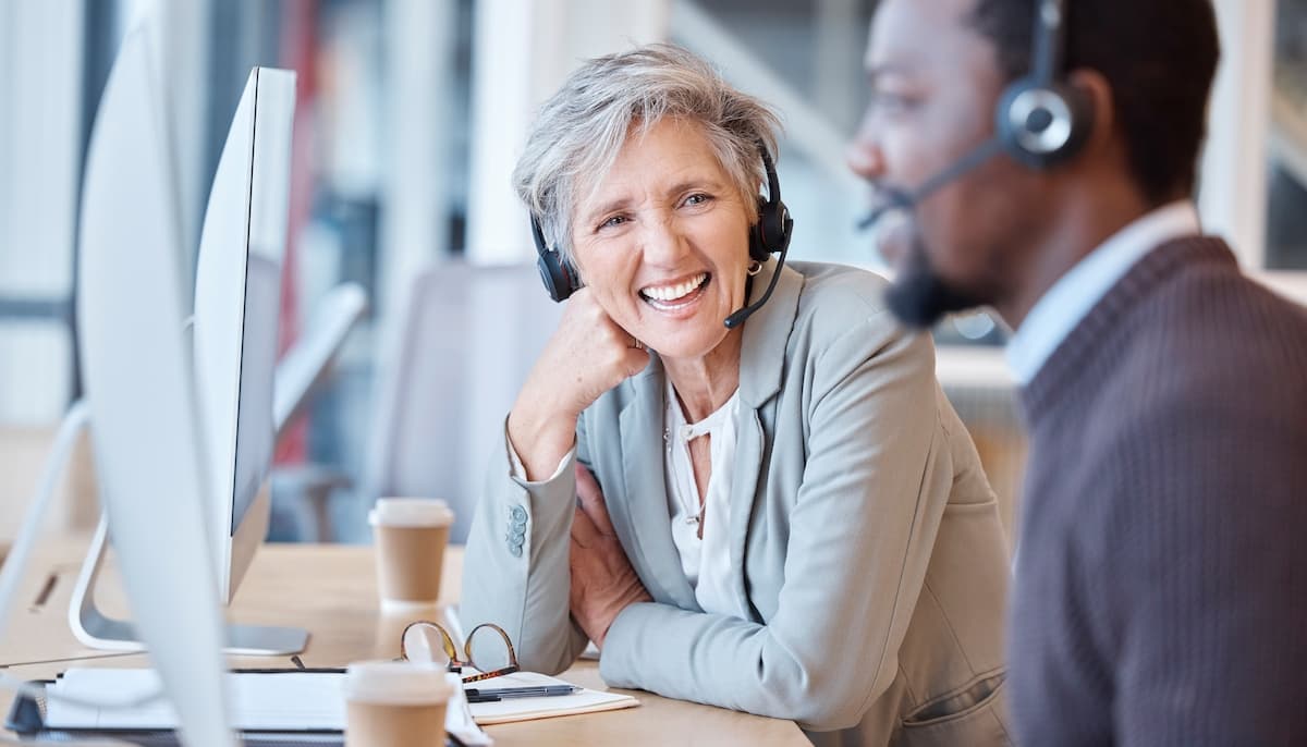 An older female call centre worker smiling with a colleague