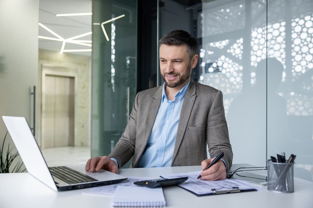 a smiling businessman at a desk looking at laptop