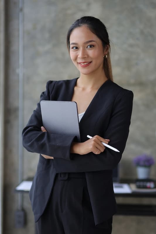 A corporate personal assistant holding a tablet and a pen in a modern office setting