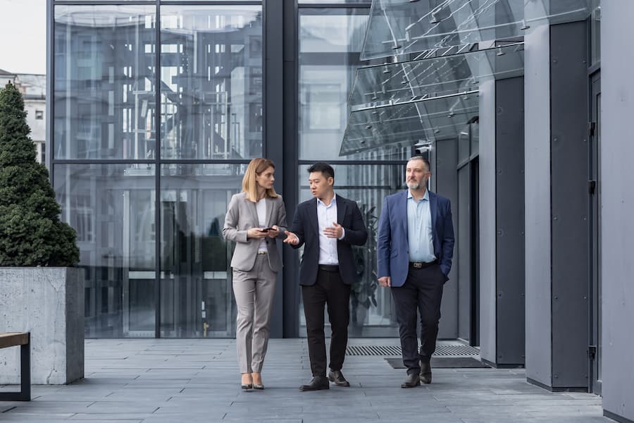 Three diverse business people walking and talking outside modern building
