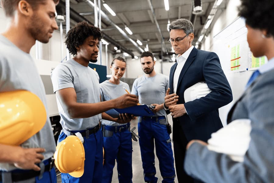 Businessman and African American factory worker reading reports in industrial building.