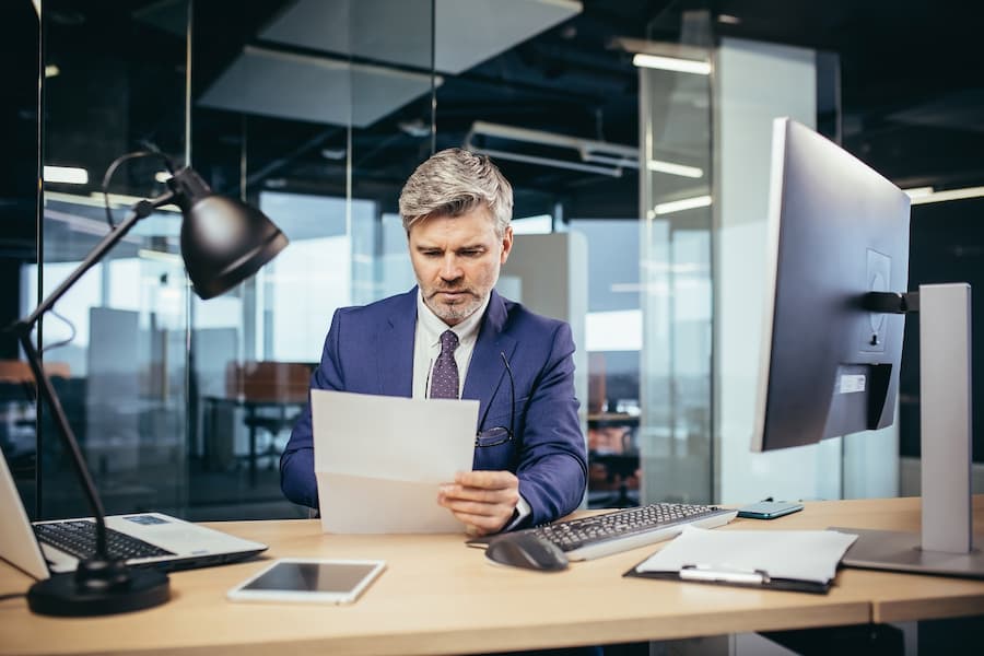 Experienced gray-haired businessman working at a computer, paperwork in the office