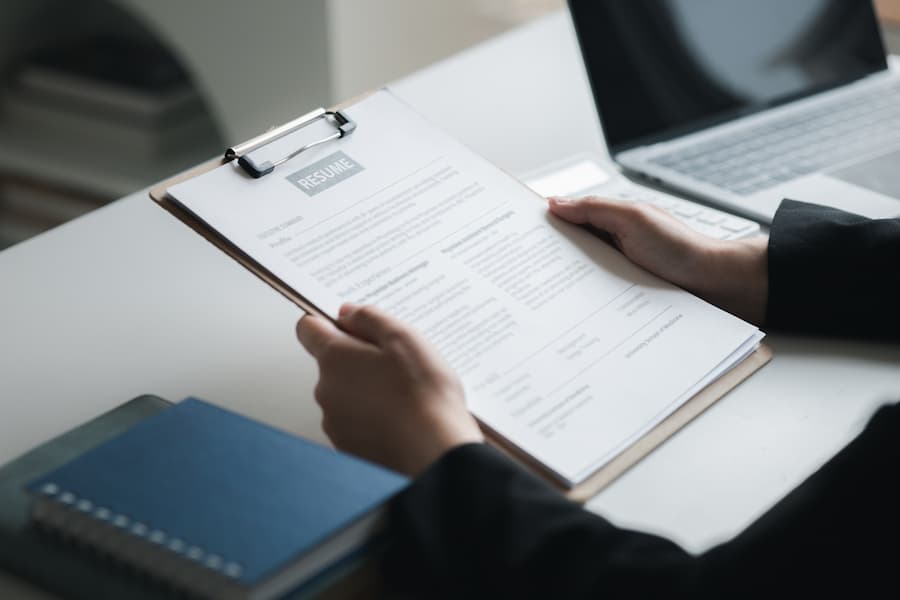 Hands Holding a Resume with Laptop and Notepad