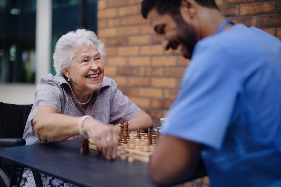 Aged care nurse playing chess and laughing with an elderly woman