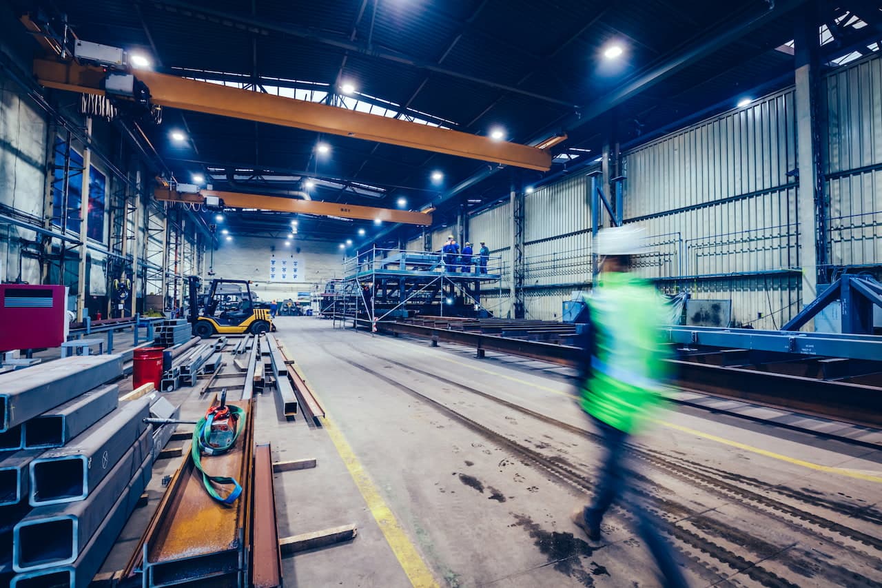 Engineer walking in large factory, blue-collar workers at work.