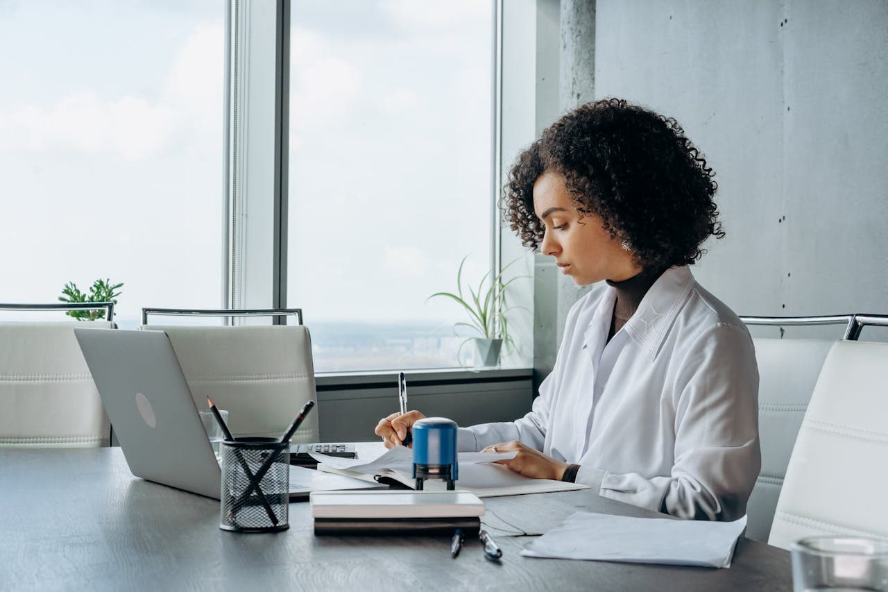 African American woman in a white shirt working at a laptop in a bright, modern office setting