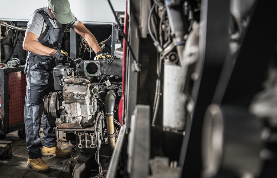 Mechanic Repairs Engine in Workshop While Wearing Gloves and Work Attire
