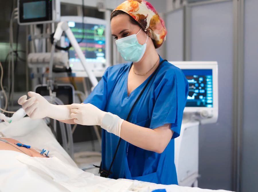 Nurse wearing surgical mask and putting on sterile gloves in hospital room