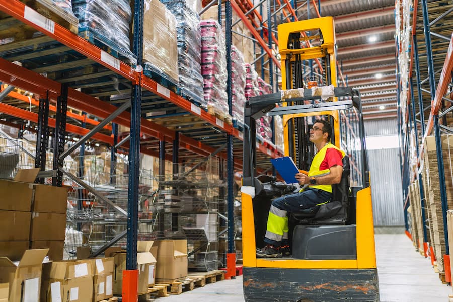Warehouse worker driving forklift and checking inventory with clipboard