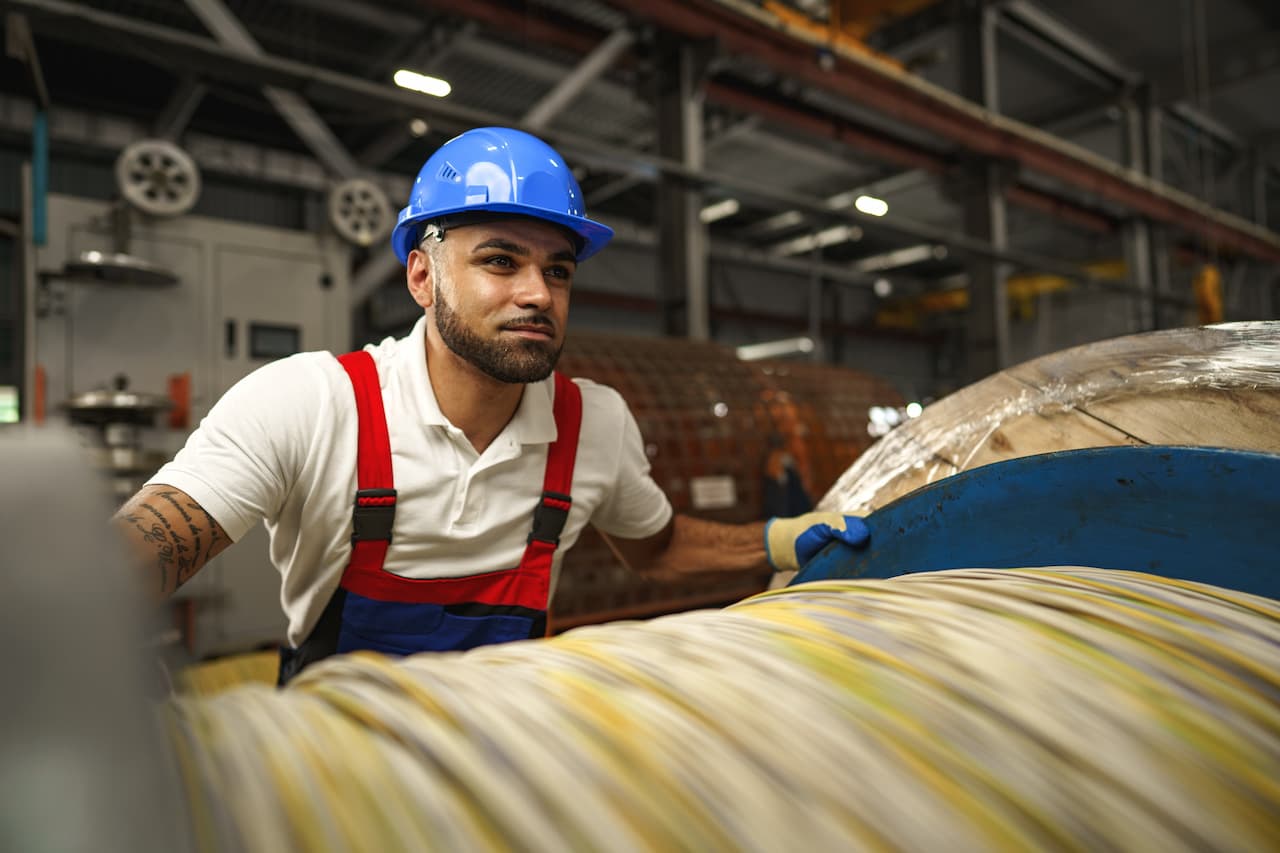 A young factory workman rolls heavy coil of electric cables
