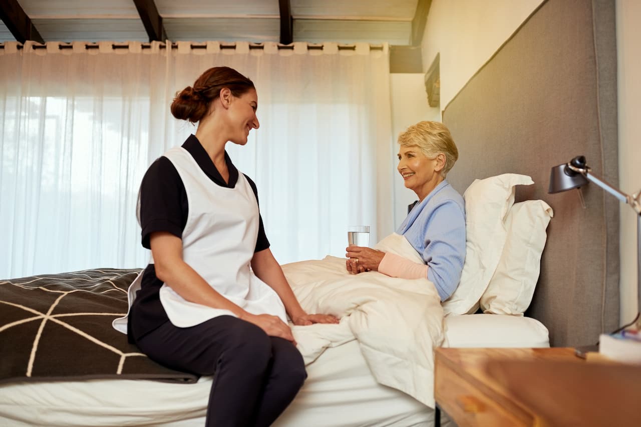 Aged care nurse with Senior Woman in Bed at Home
