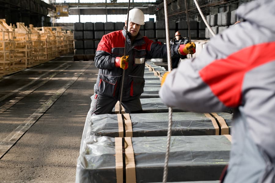 Construction Material Handlers Securing Pallet with Straps in Warehouse