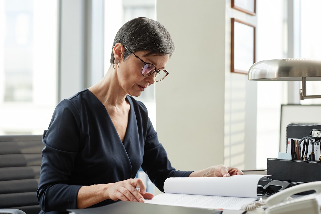 Elegant mature woman as female boss working with document at desk in office