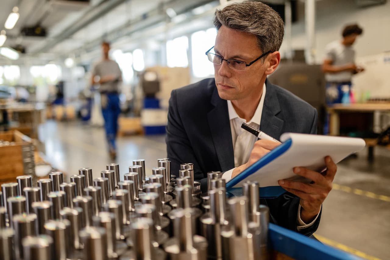 Mid adult engineer taking notes while inspecting finished steel products in a factory.