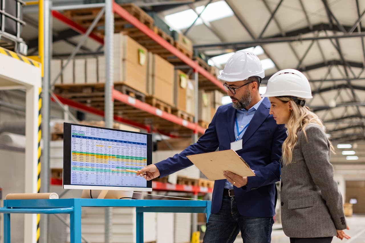 Female engineer and male project manager standing in modern industrial factory, talking about