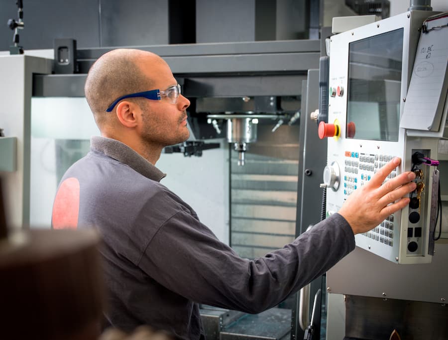 Knife factory worker operating machine control panel in workshop
