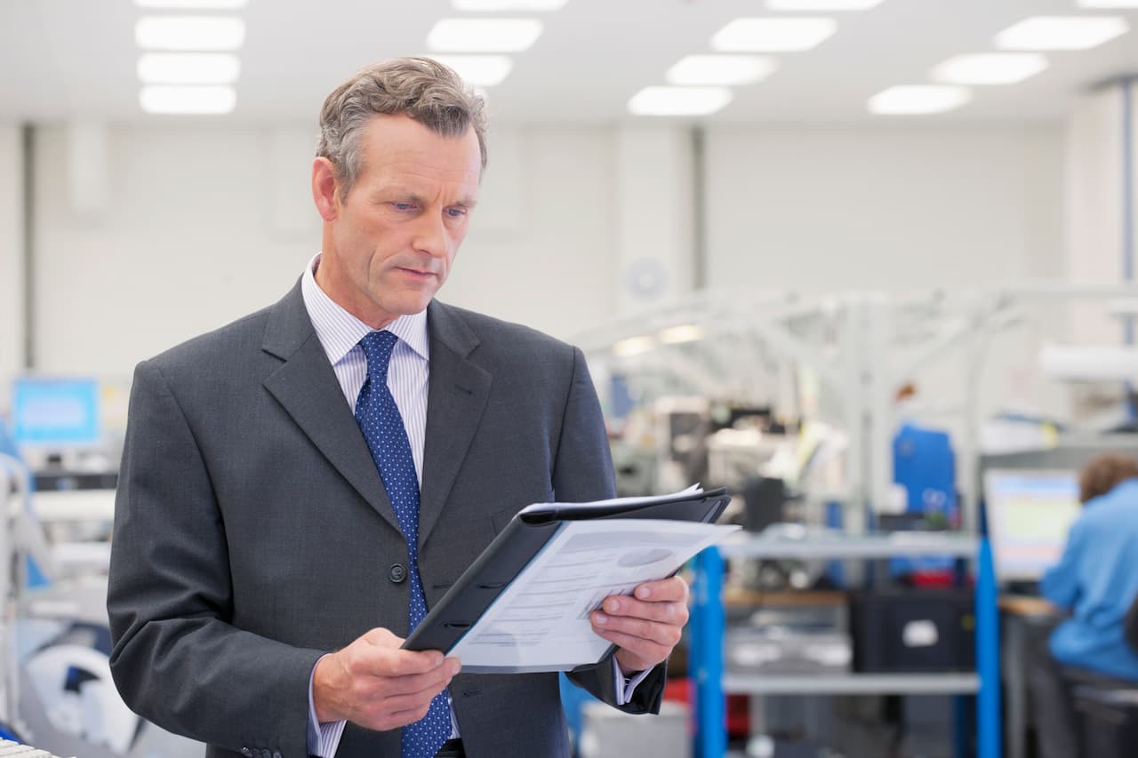 Medium Shot Of A Businessman In Suit Reviewing Paperwork In A Manufacturing Plant.