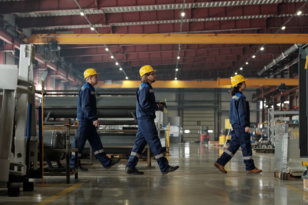 Side view of three engineers of industrial plant moving forwards while going to another workshop