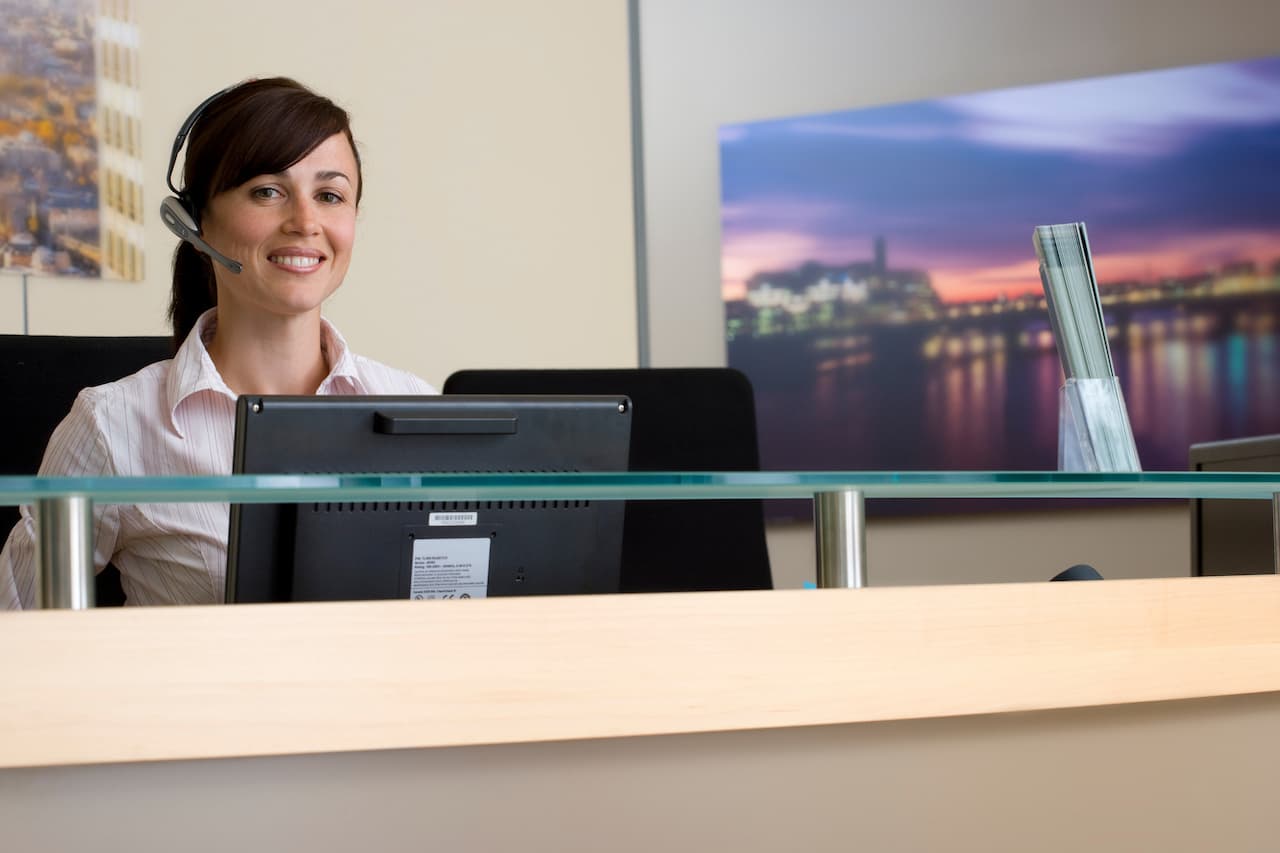 Smiling Woman at Office Reception Desk Wearing Headset
