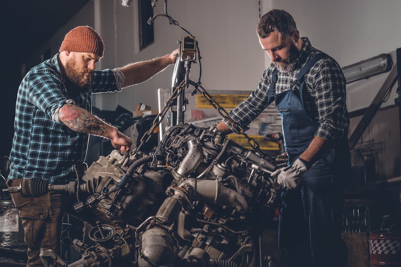 Two diesel fitters repairing engine in a garage.