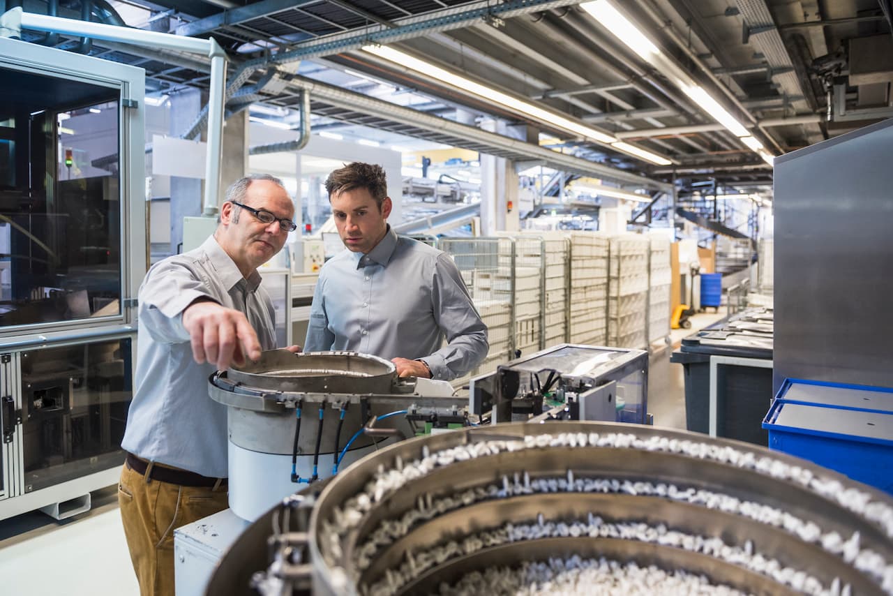 Two men in factory shop floor examining outcome of a machine