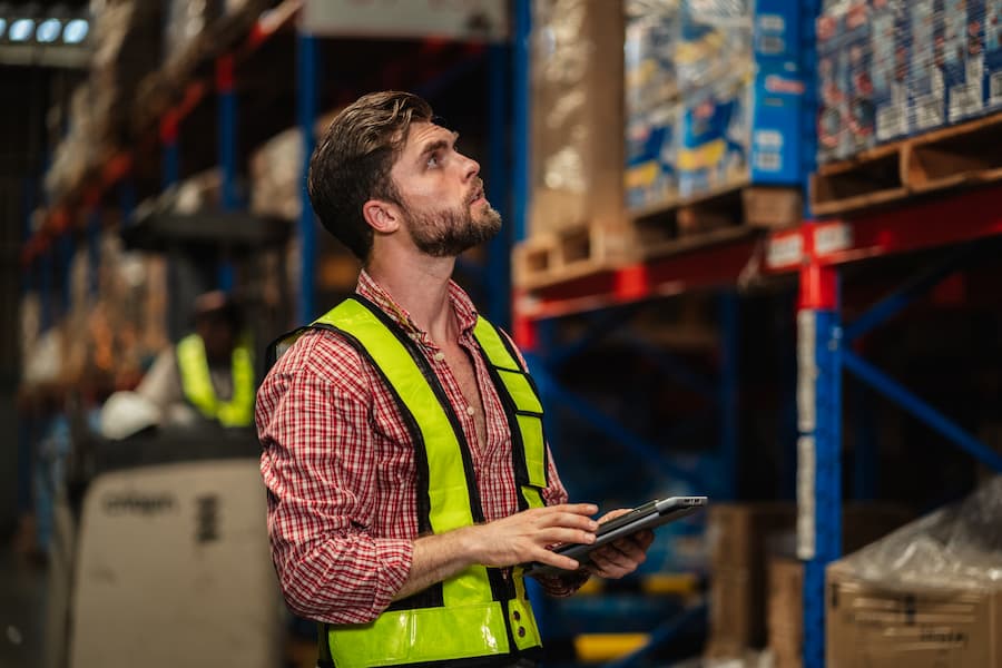 Warehouse team in safety vests checking inventory with digital tablet.
