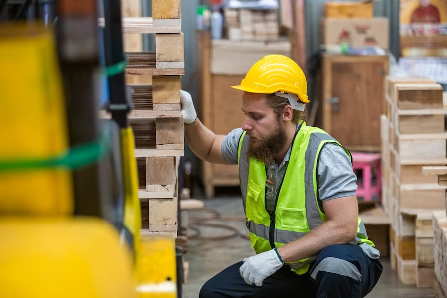 Warehouse Worker Inspecting Stacked Wooden Pallets at Work