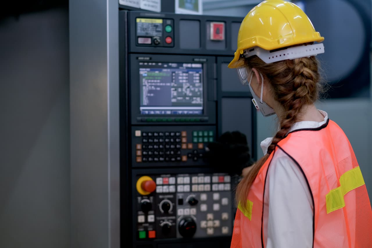 Back of factory worker woman with mask adjust button near the monitor of machine