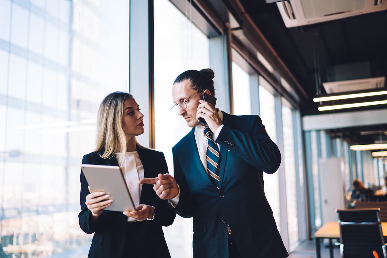 formally dressed colleagues discuss over tablet in office interior