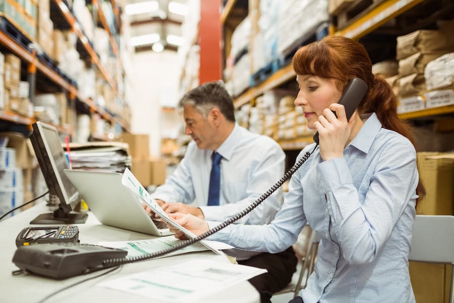 A logistics manager and administration working at desk in a large warehouse